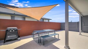 A patio with a barbecue grill, a table, and a shade sail. - HAVENVIEW TERRACES #2 | Close to beach, shops and cafes | Accom Property (TERRIGAL)