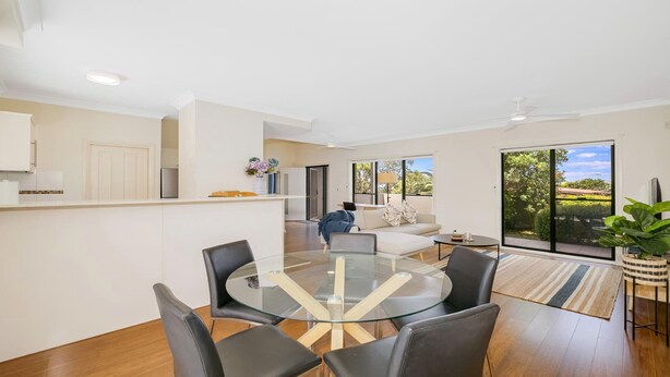 A modern living room with a glass dining table, black leather chairs, a sofa, and a large sliding glass door leading to a balcony. - HAVENVIEW TERRACES #2 | Close to beach, shops and cafes | Accom Property (TERRIGAL)