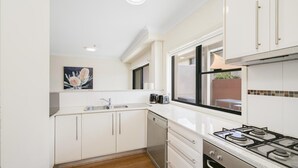 A modern kitchen with white cabinetry, a stainless steel sink, a gas stove, and a window with a view of the outdoors. - HAVENVIEW TERRACES #2 | Close to beach, shops and cafes | Accom Property (TERRIGAL)