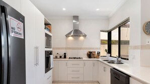 A modern kitchen with white cabinets, a stainless steel range hood, a double sink, and a dishwasher. - Summer Breeze at Avalon Beach (Wannanup)