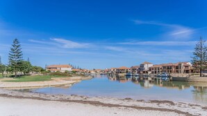 A waterfront property with a marina, buildings with red-tiled roofs, and a clear blue sky. - Summer Breeze at Avalon Beach (Wannanup)