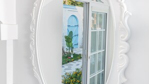 A white ornate mirror with a light fixture above it, reflecting a blue door and a garden with plants and a pathway. - Louise'in Konağı (Datça)