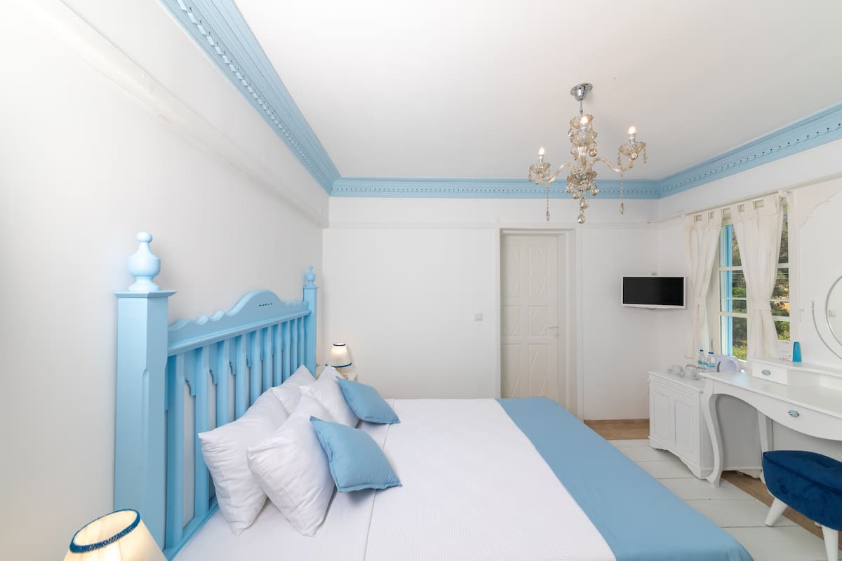 A bedroom with a bed, a desk, a TV, and a chandelier.