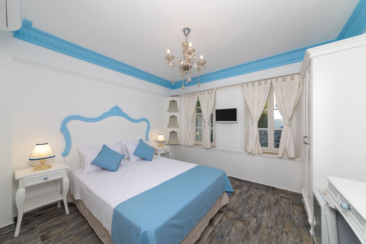 A bedroom with a bed, nightstands, a chandelier, and a TV on the wall.