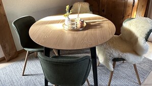 A cozy dining area with a round wooden table, two chairs, and a fluffy chair. A wooden cabinet and a lamp are in the background. - Cozy attic apartment with charm - & private balcony (Zermatt)