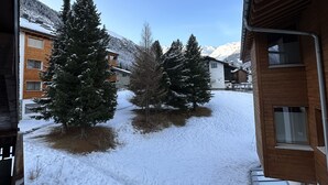 A snowy courtyard with buildings, trees, and a clear sky. - Cozy attic apartment with charm - & private balcony (Zermatt)