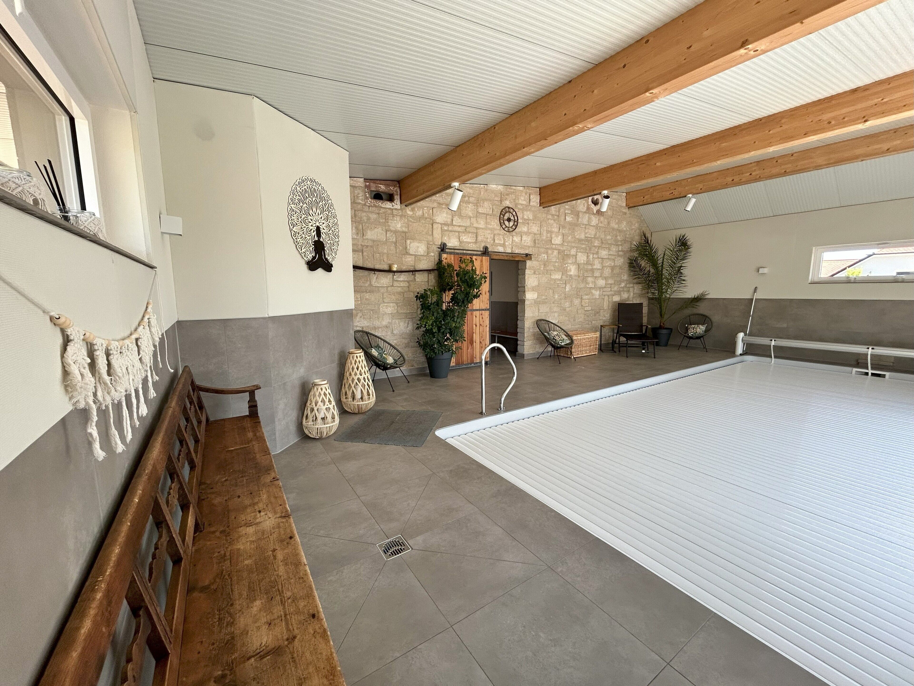 Un vaste espace intérieur doté d’une grande piscine, de murs en pierre, de poutres en bois et de différents types de mobilier.