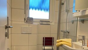 Een kleine badkamer met toilet, wastafel, douche en een raam.