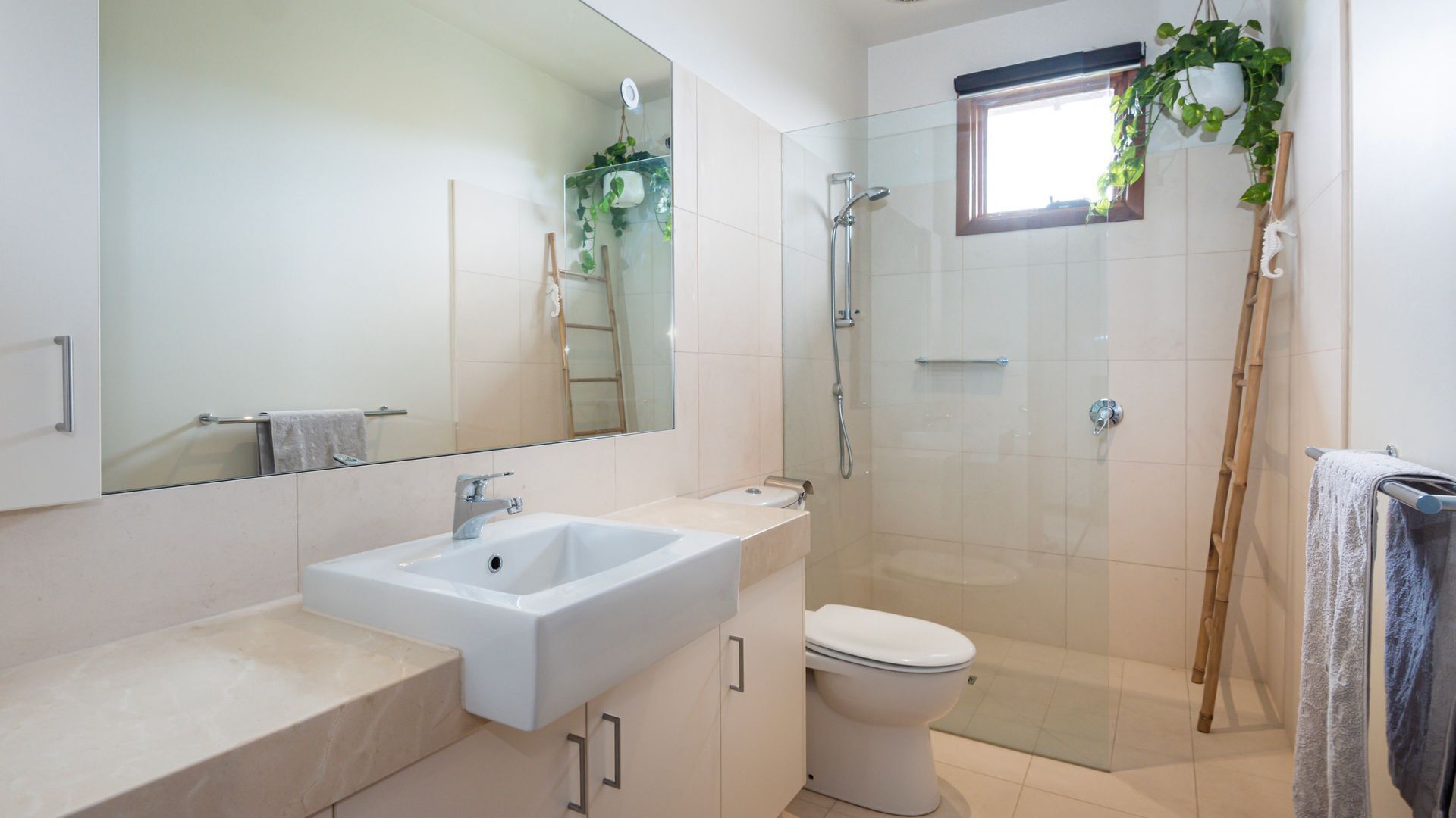 A modern bathroom with a large mirror, a sink, a toilet, and a glass-enclosed shower.