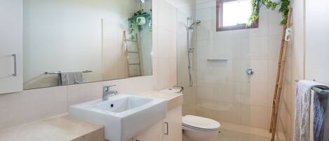 A modern bathroom with a large mirror, a sink, a toilet, and a glass-enclosed shower.