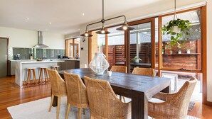 A modern kitchen with a central island, wooden flooring, and a dining area with wicker chairs and a large table. - Pet Friendly - Bayside Oasis in Highett (Highett)