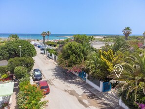 A street view of Villa Coralia with a clear view of the beach, parked cars, and lush greenery. - 2 bedrooms - 1 bathroom with shower - air conditioning - wifi - parking space (Carovigno)