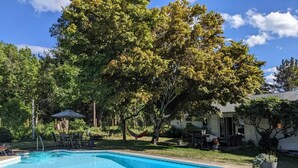 A rectangular swimming pool with a clear blue water surface, surrounded by a grassy area with trees and a house in the background.