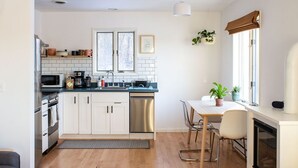 A modern kitchen with white cabinets, a stainless steel dishwasher, and a dining area with a white table and chairs.