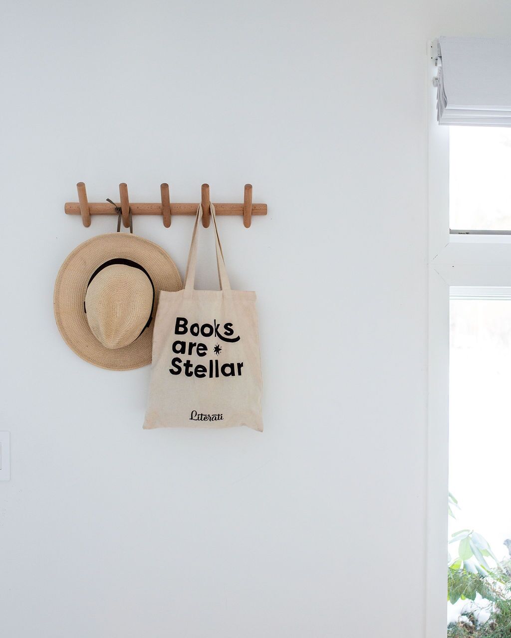 A wall-mounted hat rack with a straw hat and a tote bag with text.