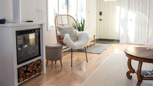 A cozy living room with a fireplace, a wicker chair, a round wooden table, and a white door.