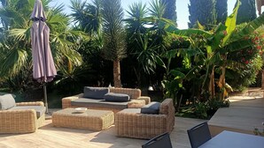 An outdoor patio with wicker furniture, a table, and a variety of tropical plants. - Pretty villa with sea view and pool **** (Bormes-les-Mimosas)