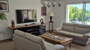 A living room with a sofa, coffee table, TV, and a view of the outdoors. - Pretty villa with sea view and pool **** (Bormes-les-Mimosas)