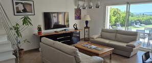 Relax in this stylish living room with a flat-screen TV, comfortable sofas, and a glass door leading to an outdoor area with a view.