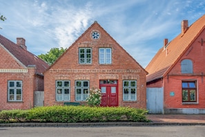 A red brick building with a red door, multiple windows, and a small garden in front. - Vacation home Hus rode Dör for up to 5 people (Oldenswort)