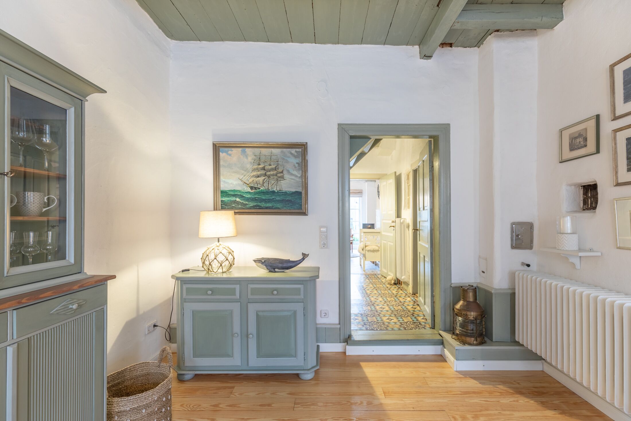A hallway with a cabinet, a lamp, a painting, and a radiator.