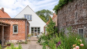 A traditional brick house with a white facade, a stone pathway, and a garden with various plants and flowers. - Vacation home Hus rode Dör for up to 5 people (Oldenswort)