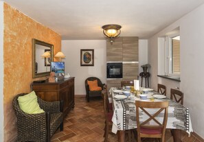 A dining area with a table set for four, a wicker chair, a wooden cabinet, and a framed picture on the wall.