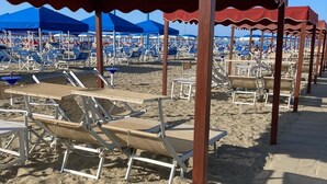 Una playa con filas de tumbonas bajo toldos rojos, dispuestas en línea.
