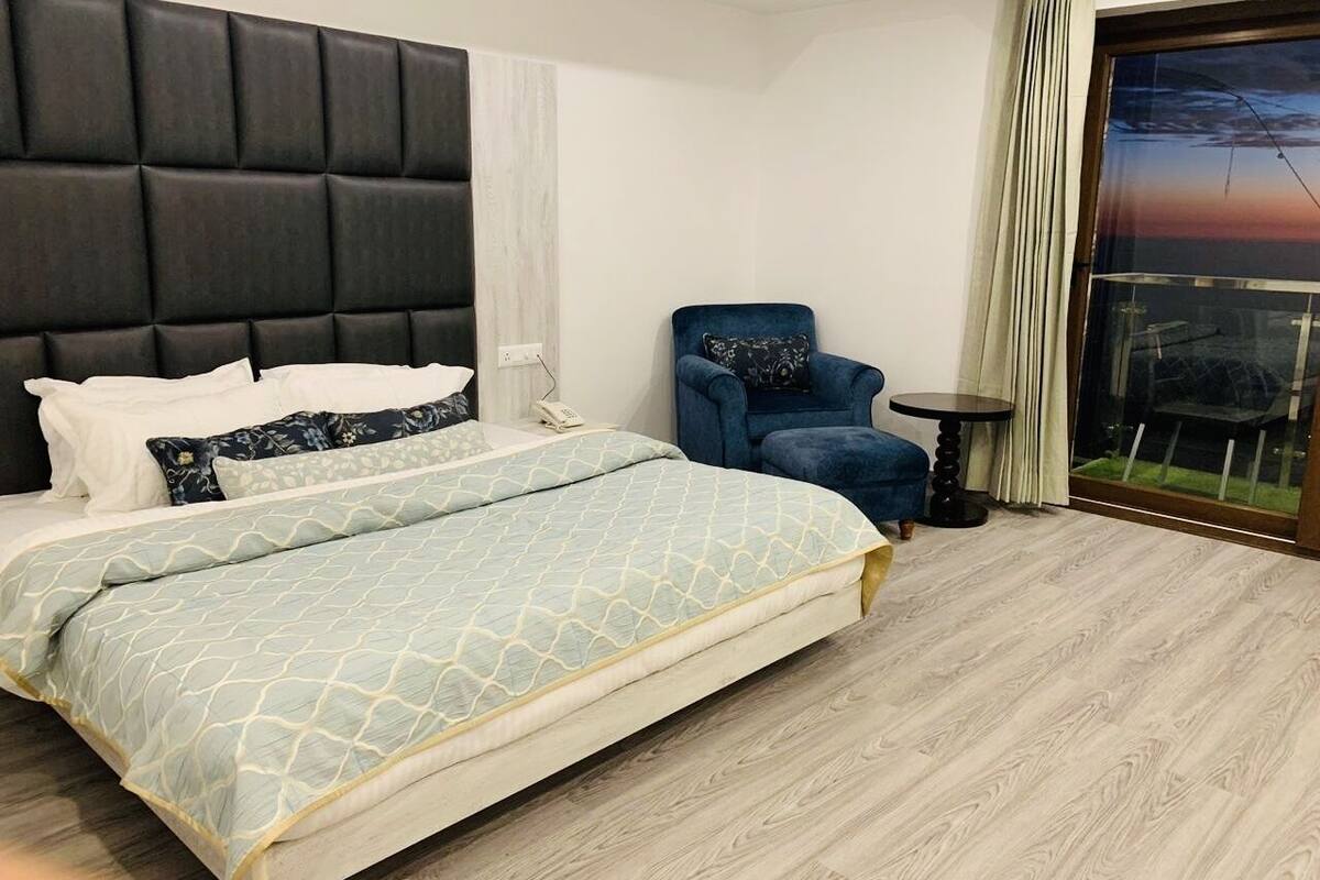 Et hotelværelse med en seng, en stol, et lille bord og udsigt til det fri.