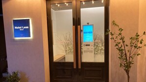 Entrada de hotel con un cartel digital, una recepción y una pequeña planta de interior.