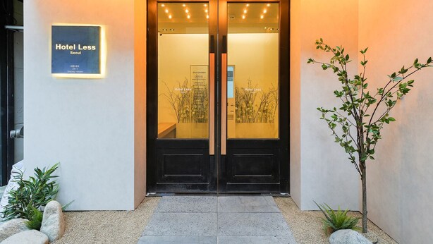 Entrada de hotel con puertas dobles, un cartel que dice "Hotel Less Seoul" y una planta pequeña a la derecha.