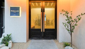 L’entrée d’un hôtel, avec une porte à deux battants, une enseigne indiquant « Hôtel Less Seoul » et une petite plante placée à droite.
