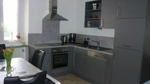 A modern kitchen with grey cabinets, a stainless steel range hood, a built-in oven, and a coffee maker on the countertop. - Geranium Apartment 3* (Colmar)