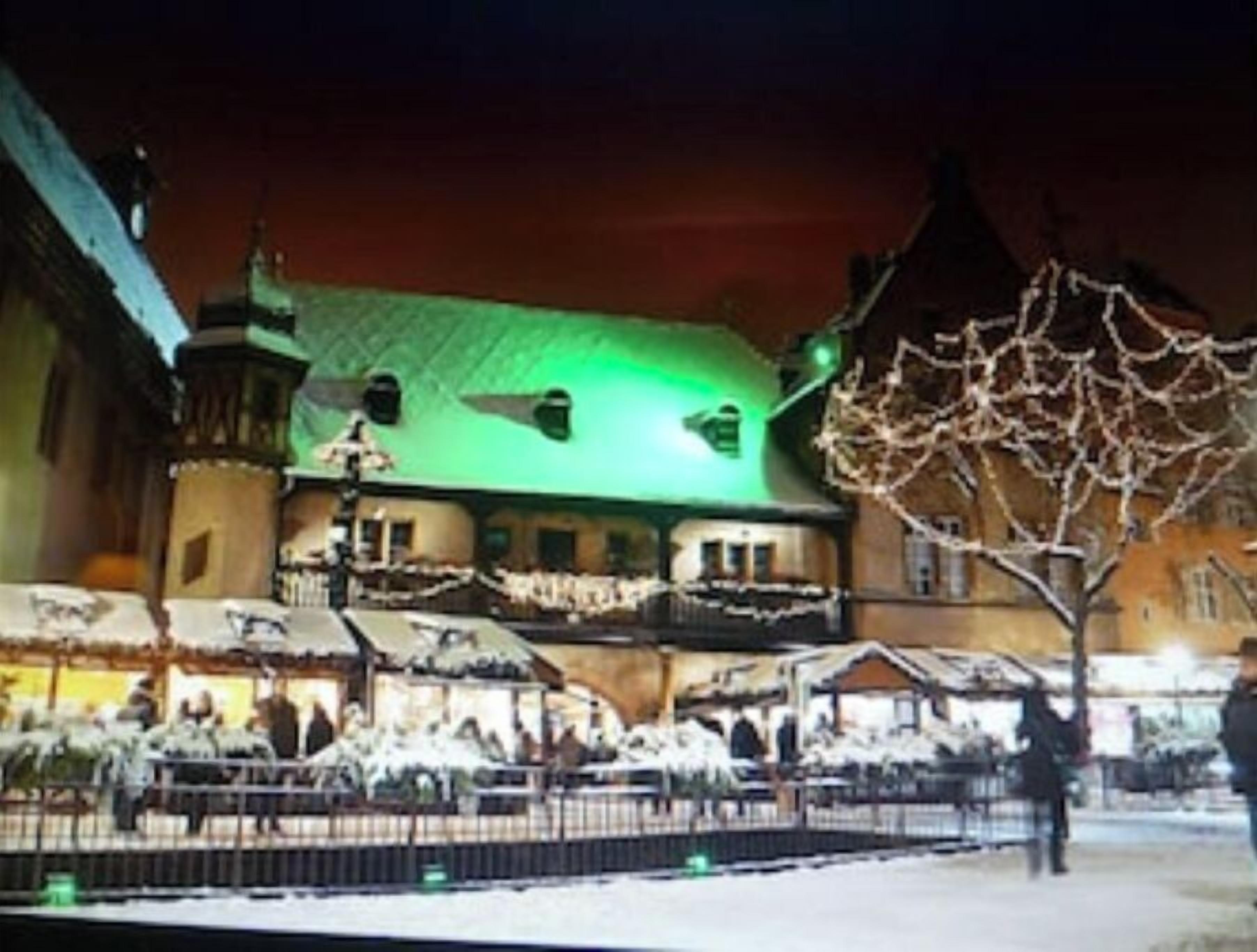 Un edificio histórico con techo iluminado en verde, un patio cubierto de nieve y un estilo arquitectónico europeo tradicional.