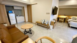 Une chambre d’hôtel compacte comprenant un coin cuisine, un canapé, une table ronde, un banc, une télévision et un lit.