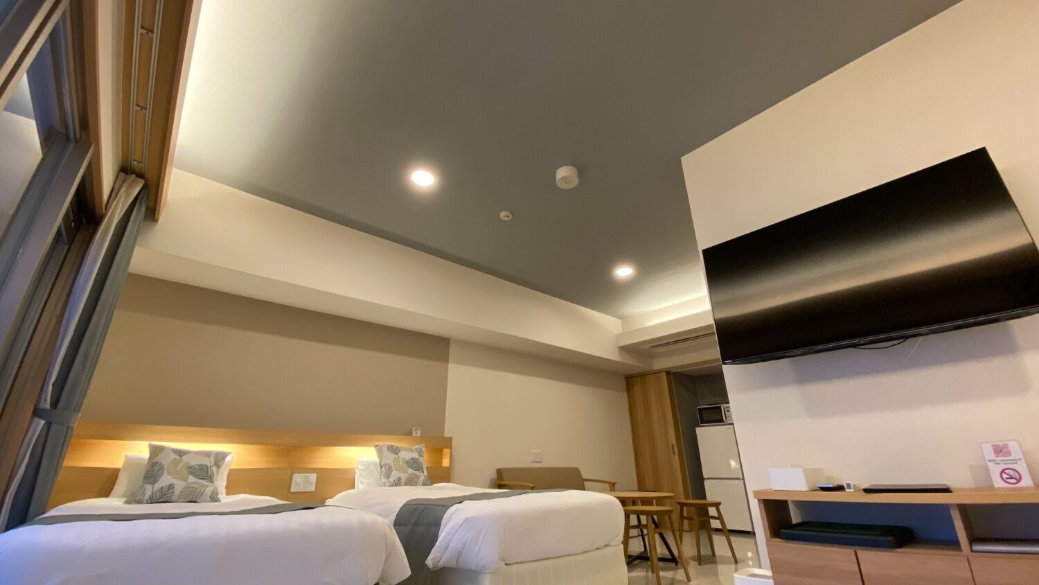 A hotel room with two beds, a desk, a chair, a flat-screen TV, and a microwave.