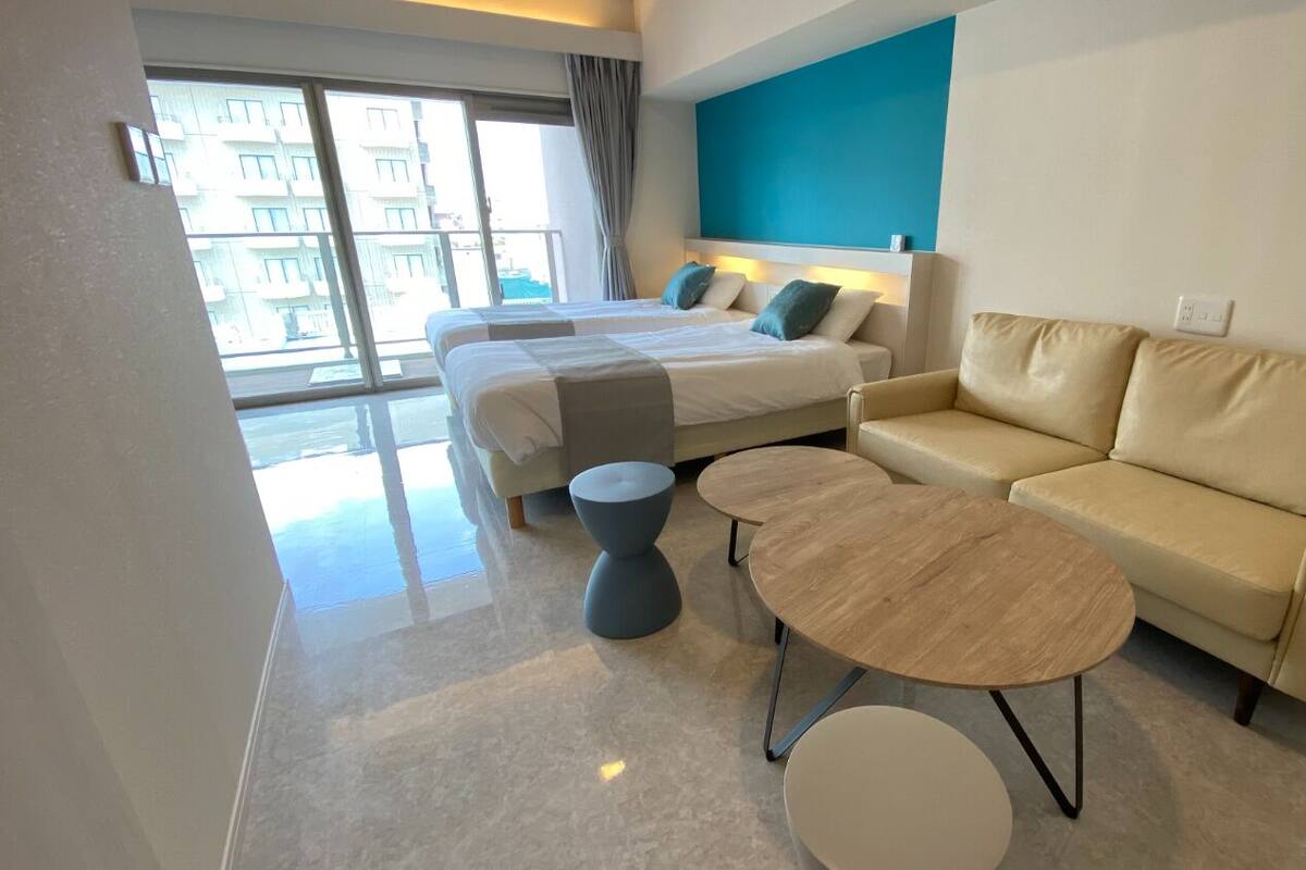 Une chambre d’hôtel moderne avec deux lits, un canapé, une table basse ronde et une petite table d’appoint.