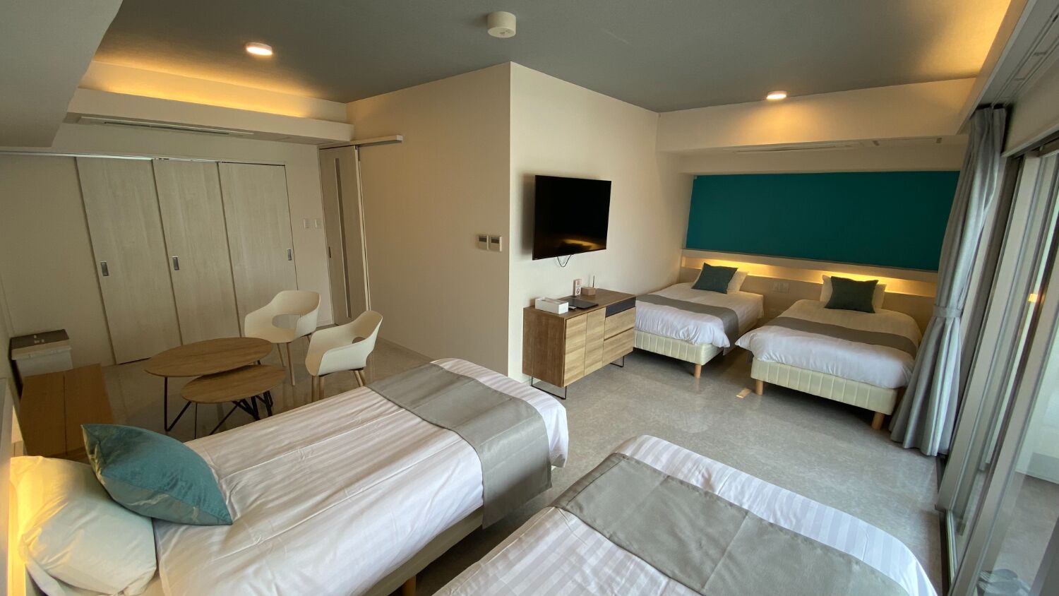 A hotel room with two single beds, a desk with a flat-screen TV, a small table, and a chair.