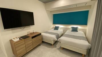 Une chambre moderne avec deux lits, un téléviseur à écran plat, une commode en bois et un mur d’accent de couleur turquoise.