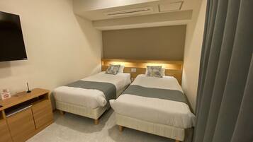 A hotel room with two beds, a wooden nightstand, a flat-screen TV, and a ceiling-mounted air conditioning unit.