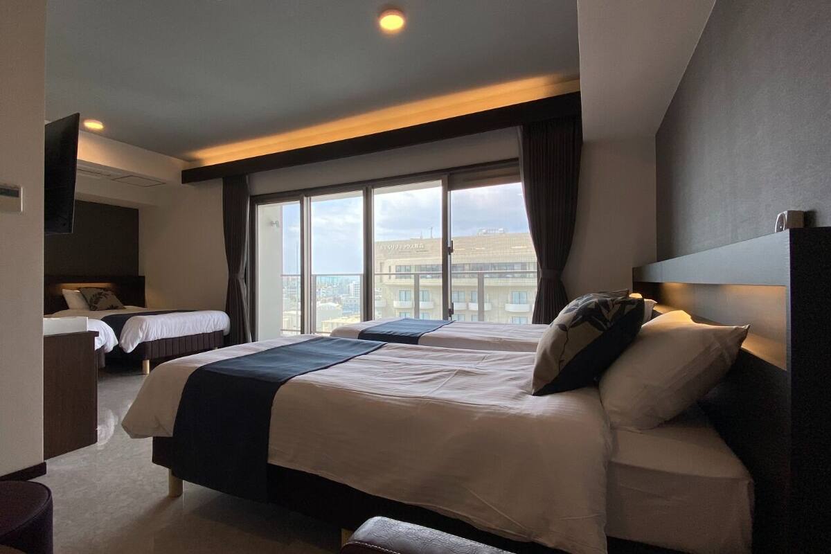 Une chambre d’hôtel moderne avec deux lits, une grande fenêtre donnant sur la ville et un coin salon séparé.