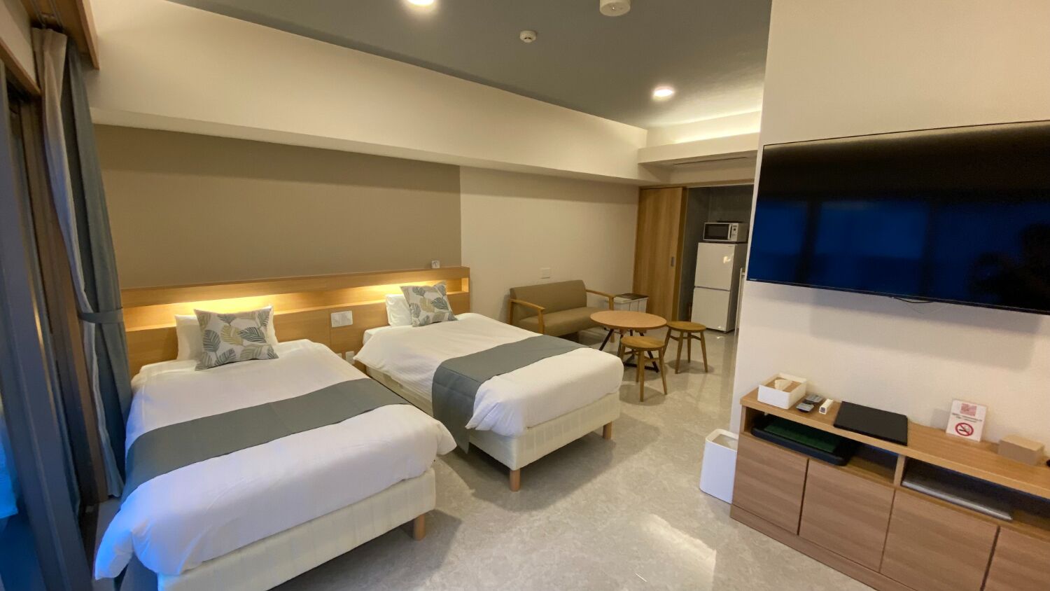 Una habitación de hotel con dos camas, un escritorio, una silla, un televisor y un microondas.