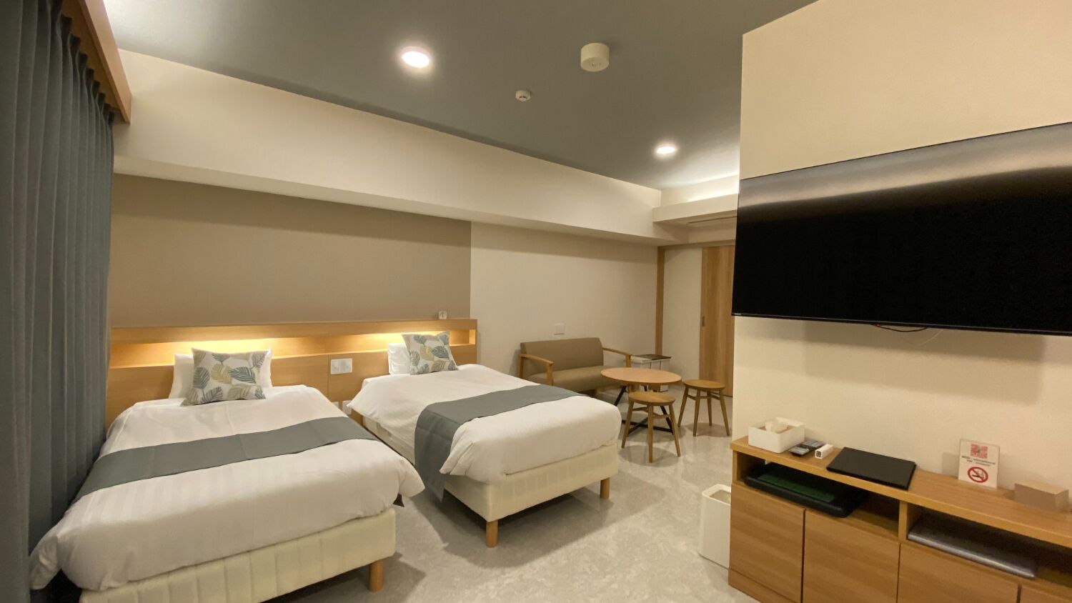 A hotel room with two beds, a desk, a chair, a TV, and a small table.