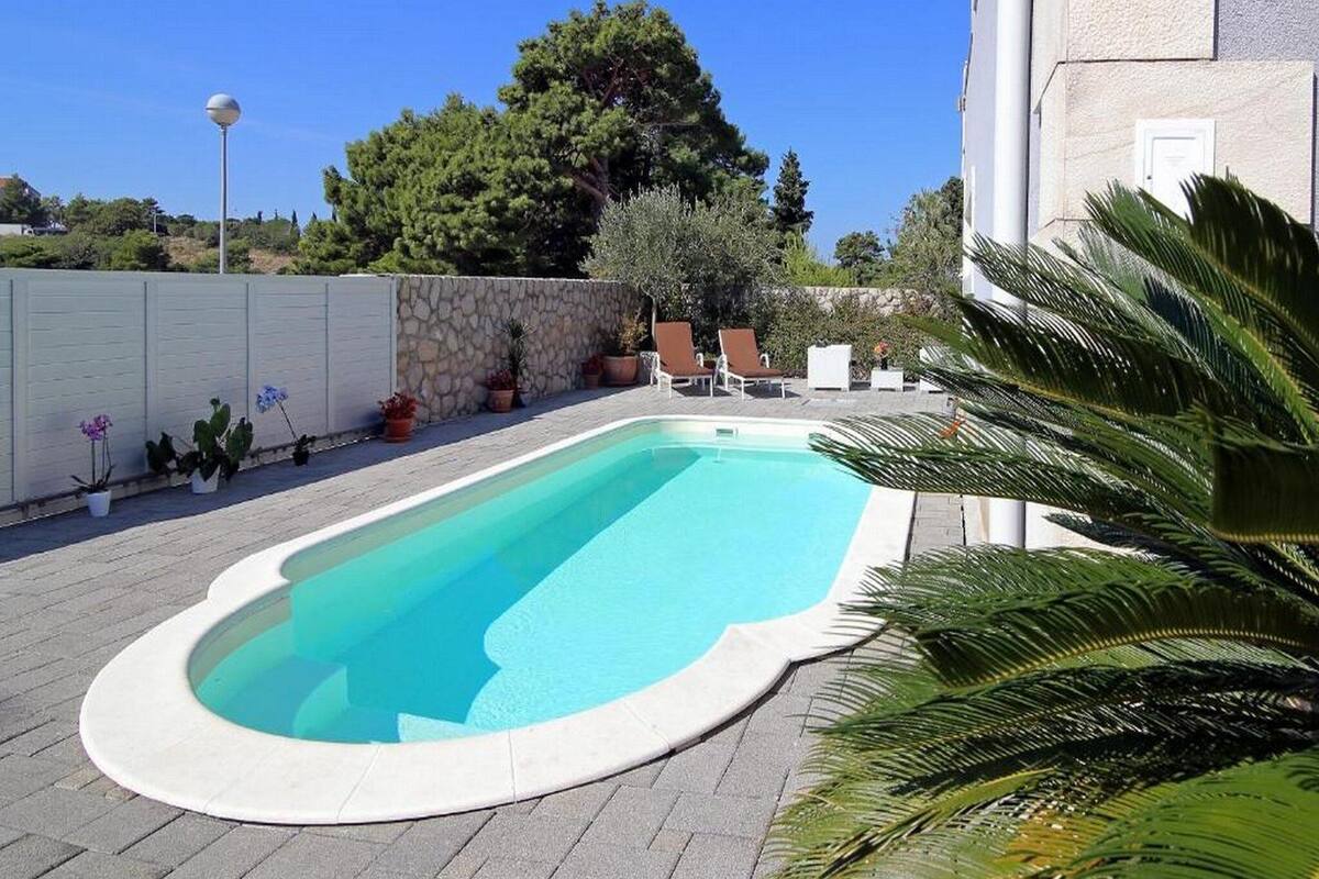 Piscina rectangular con borde blanco, rodeada por un muro de piedra y plantas en macetas.