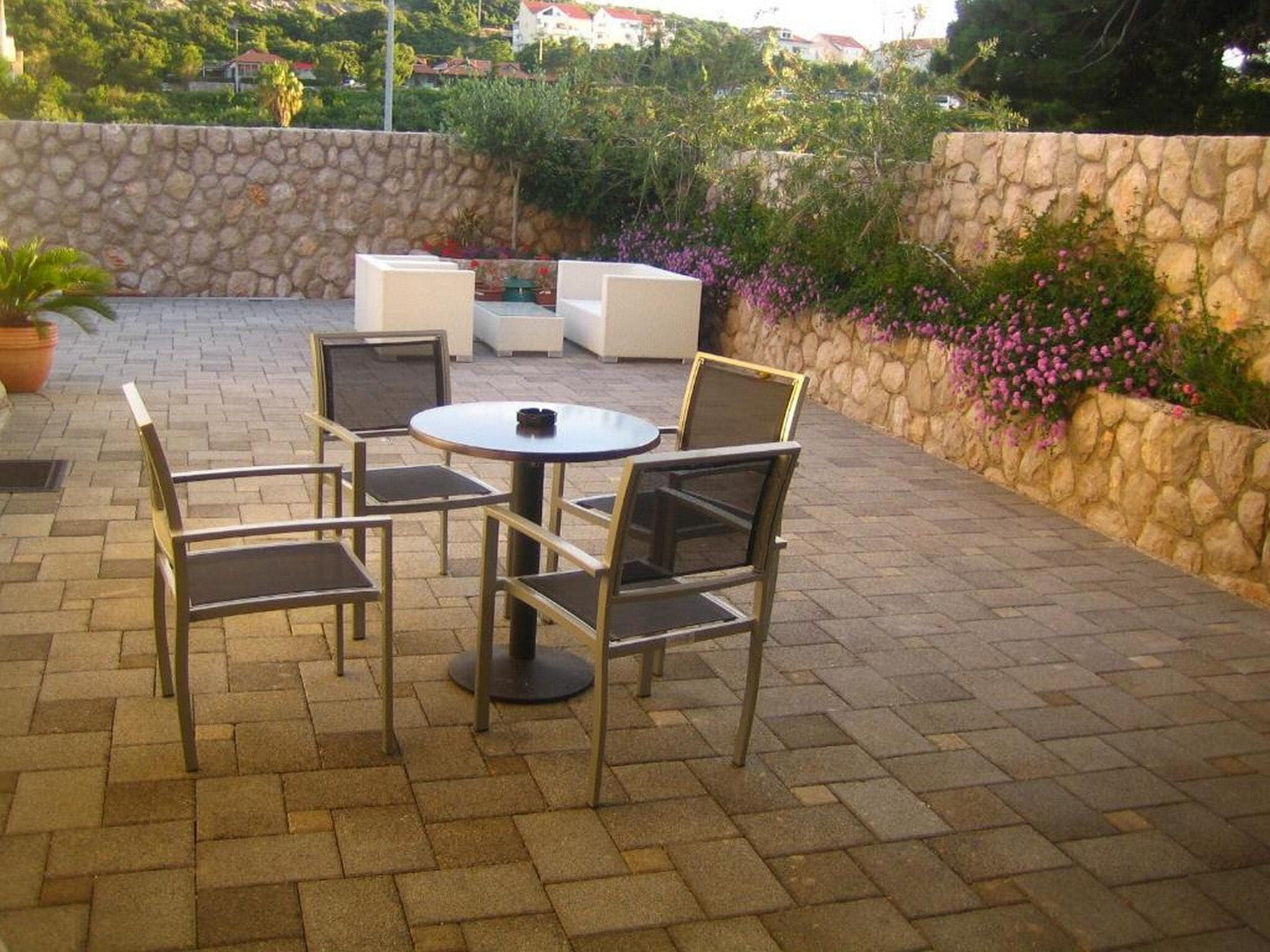 Un patio exterior con una mesa redonda y seis sillas, rodeado de muros de piedra y plantas en macetas.