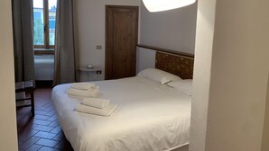 Ein Hotelzimmer mit Bett, einer runden Deckenleuchte, einem Fenster mit Vorhängen und einer Tür.