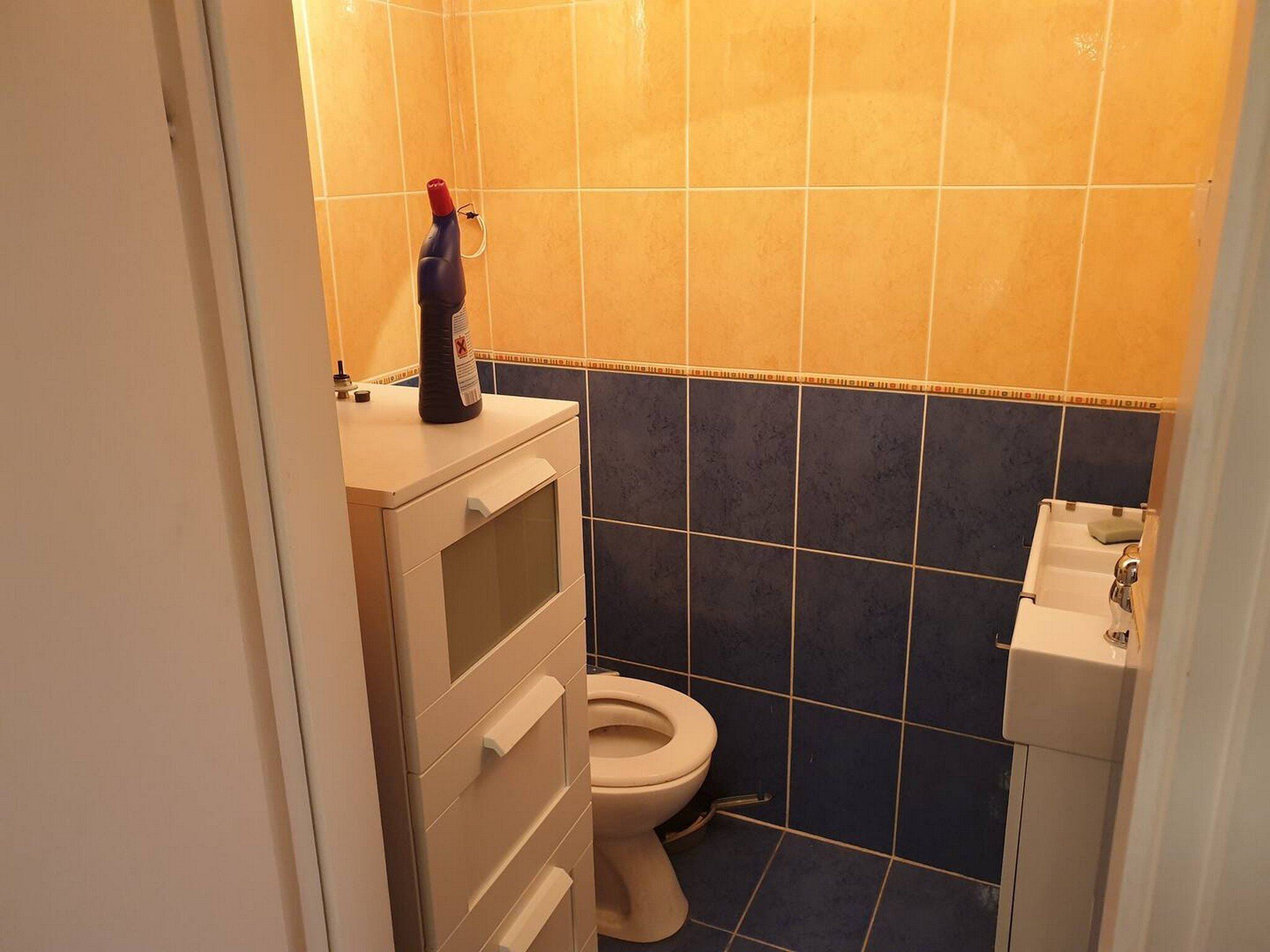 Et lille badeværelse med toilet, vask og et skab med en flaske ovenpå.