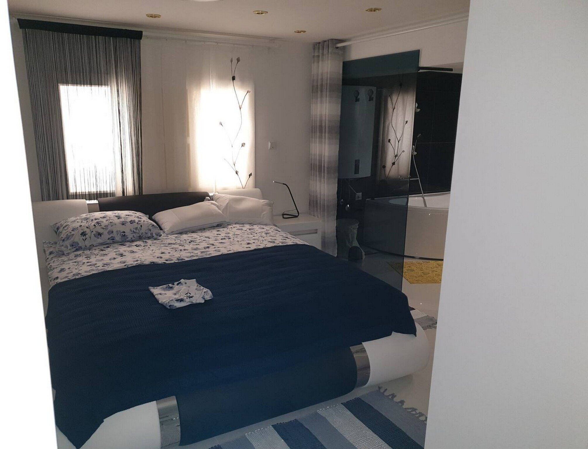 A modern bedroom with a large bed, a bathroom with a bathtub, and a view of the city.