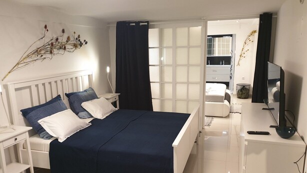 A bedroom with a bed, bedside tables, a desk with a chair, a TV, and a bathroom visible through an open door. - Apartment Vinko, Center (Zagreb)