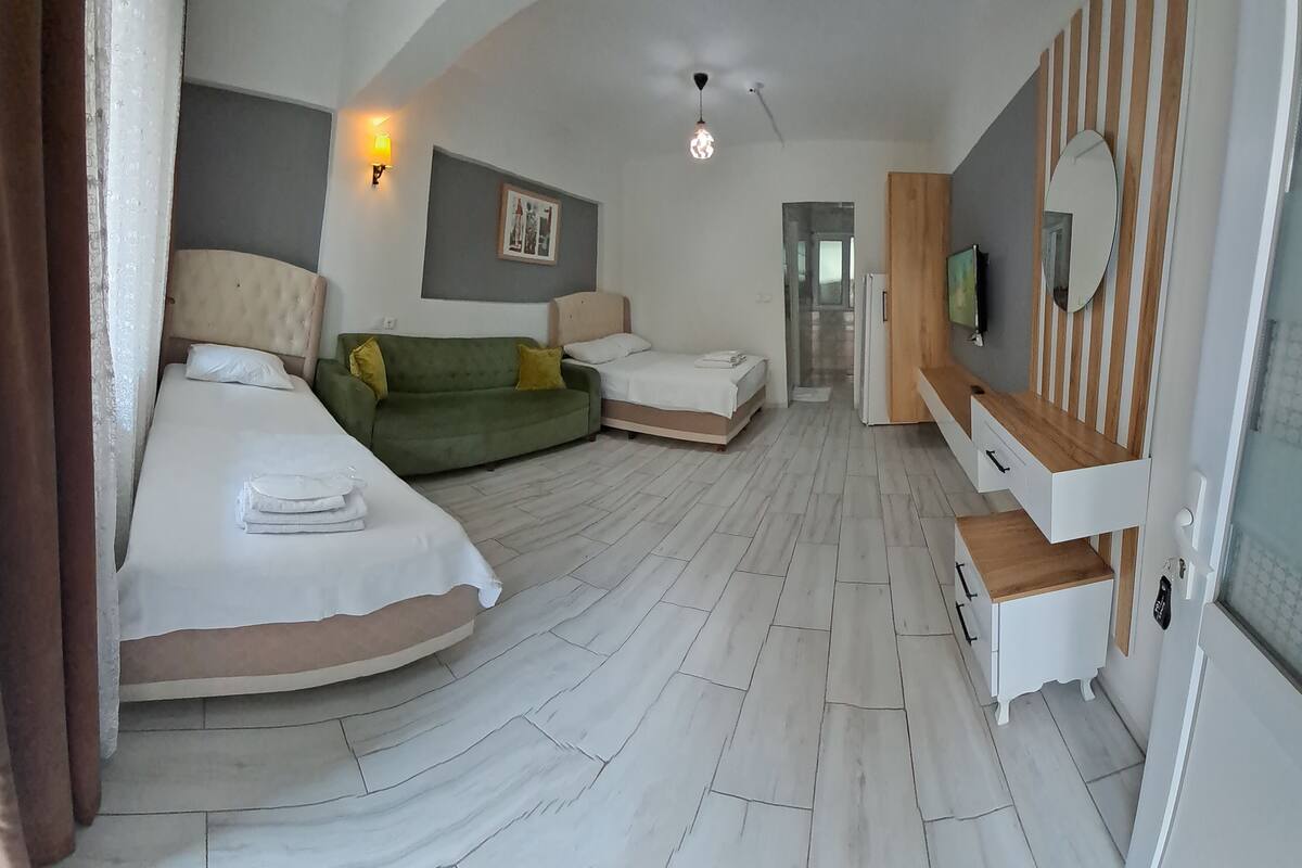 A hotel room with two beds, a green sofa, a wooden TV stand, and a tiled floor.